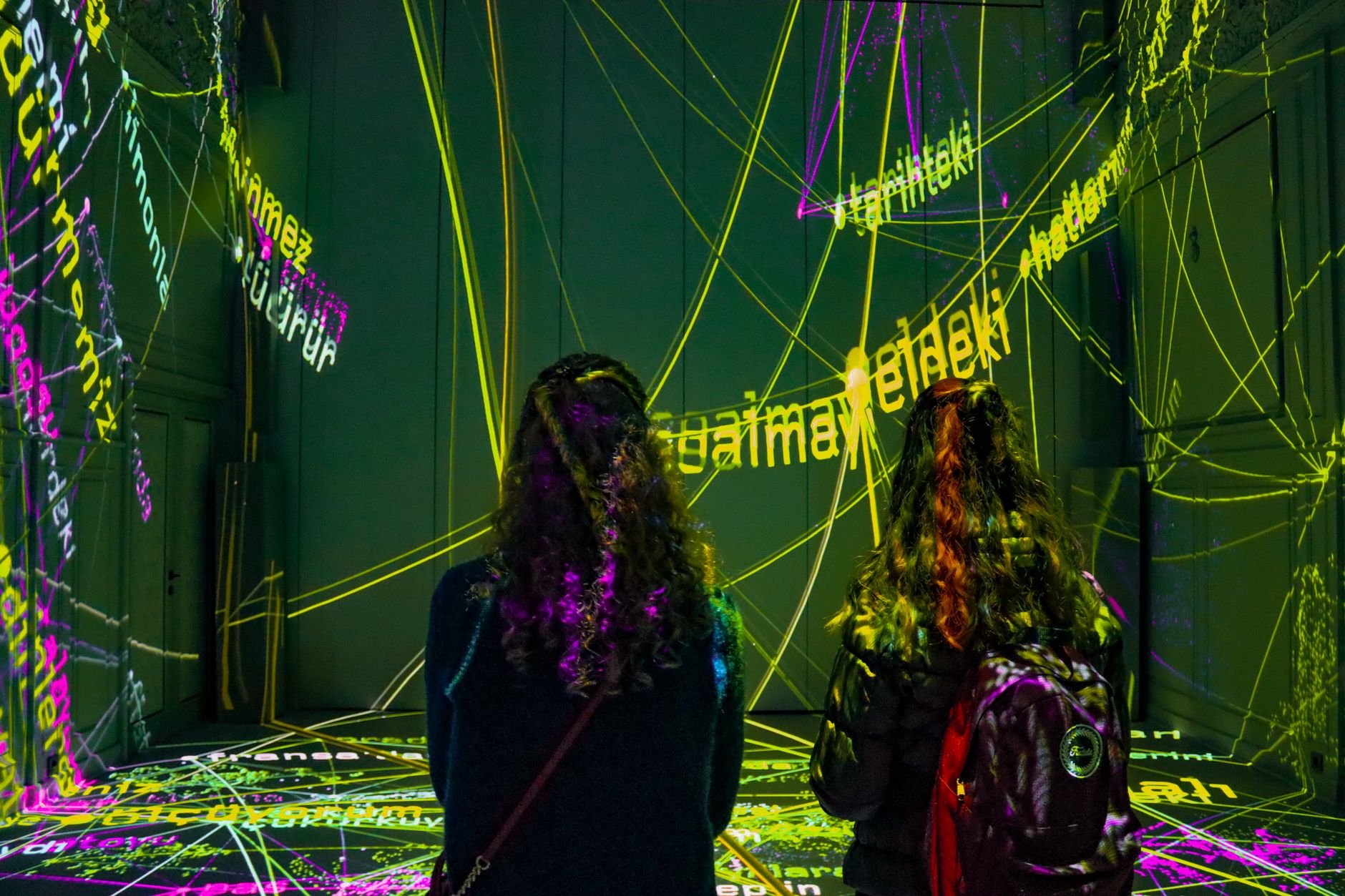 Two visitors experience a dynamic text projection installation in a darkened gallery space