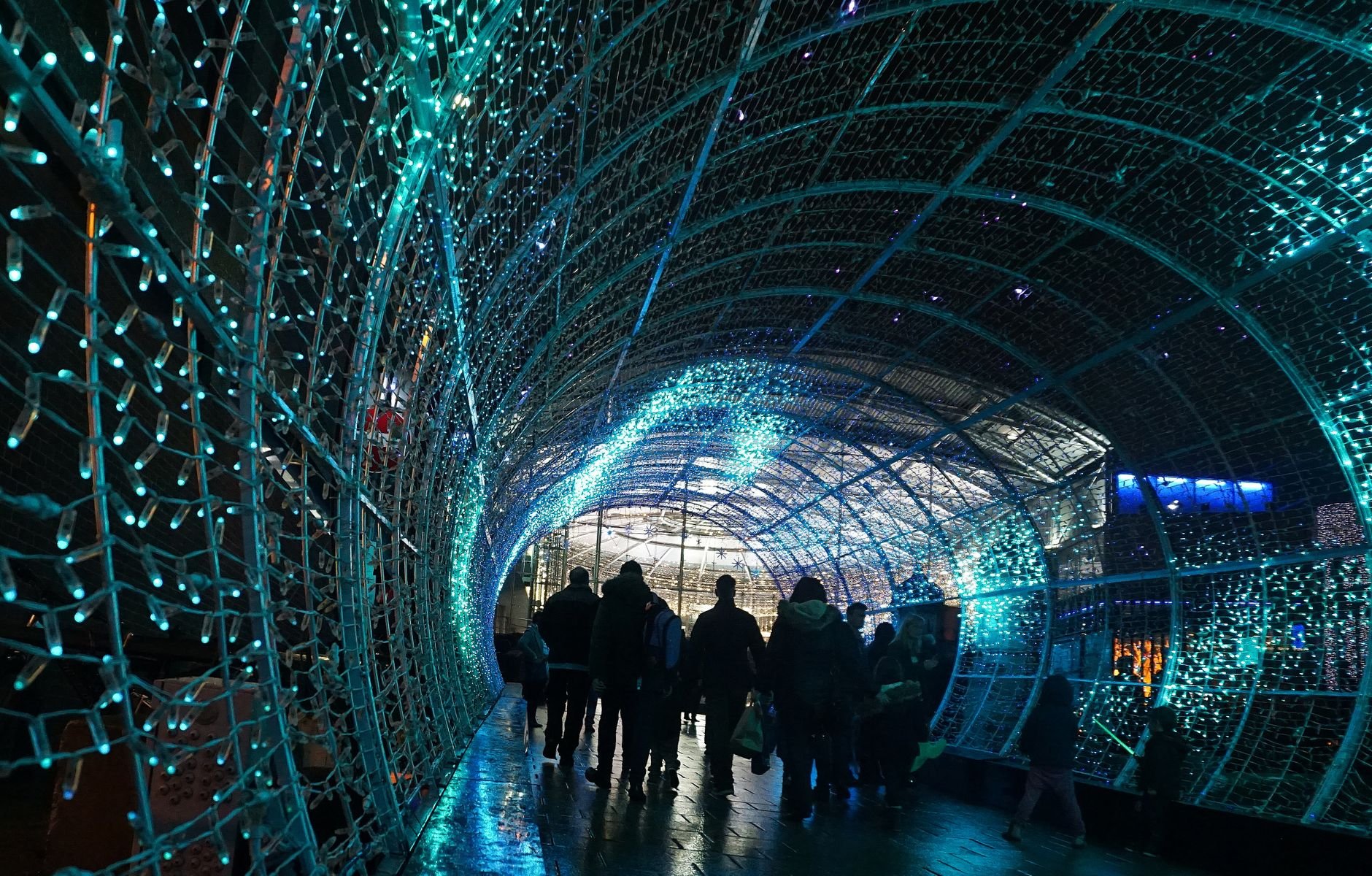 Silhouettes walking through a vibrant festive light tunnel at night